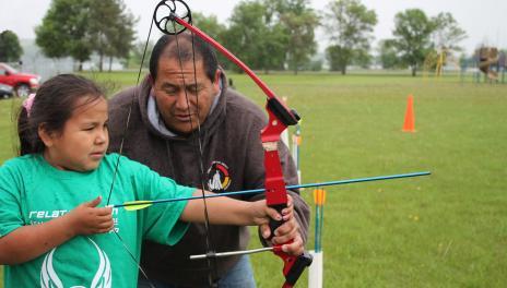 A 4-H volunteer helps a 4-H kid practice archery