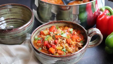 Stuffed Pepper Soup in a large cup on table next to red and green peppers