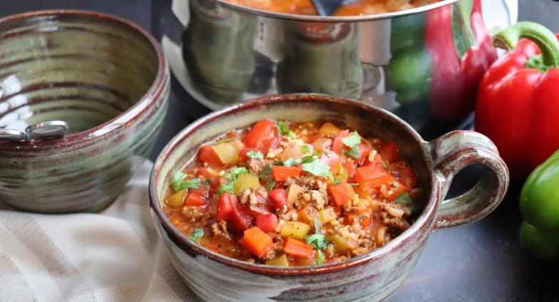 Stuffed Pepper Soup in a large cup on table next to red and green peppers